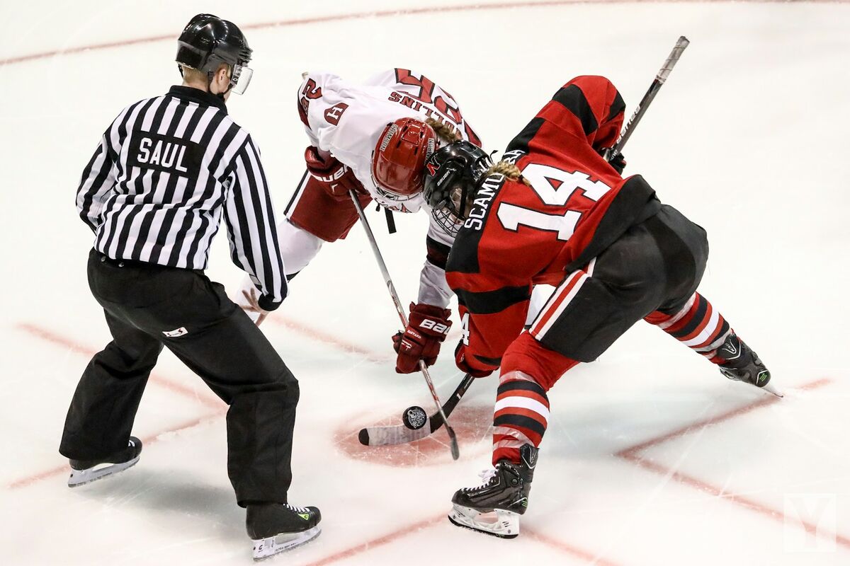 Two hockey players taking a faceoff in front of the referee